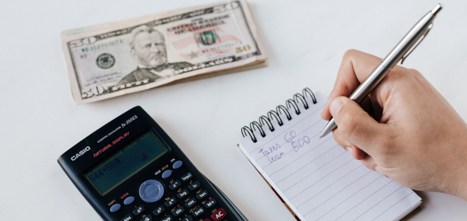 A person writing on a paper next to a calculator and money