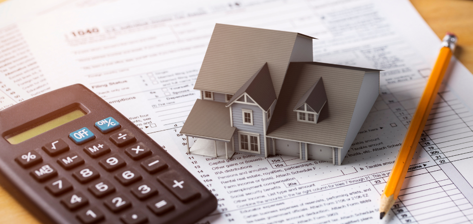 A model of house, a calculator and a pencil on top of tax papers