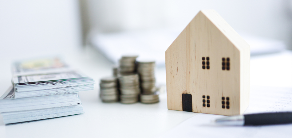 A wood shape of a house next to coins and dolllars